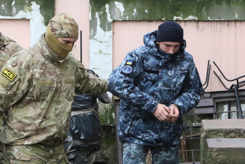 Maskovaný příslušník ruské tajné služby FSB eskortuje zajatého ukrajinského vojáka k soudu v krymském Simferopolu (úterý 27. listopadu). Foto: Pavel Rebrov, Reuters