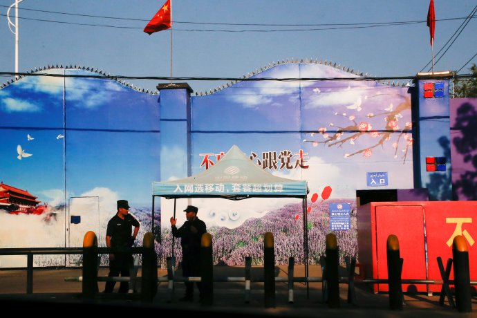 Bezpečnostní jednotky střeží vstup do internačního centra v sinťiangském okrese Chuo-čcheng nedaleko hranice s Kazachstánem (září 2018). Bránu lemuje ostnatý drát, propagandistické malby a slogany KS Číny. Foto: Thomas Peter, Reuters