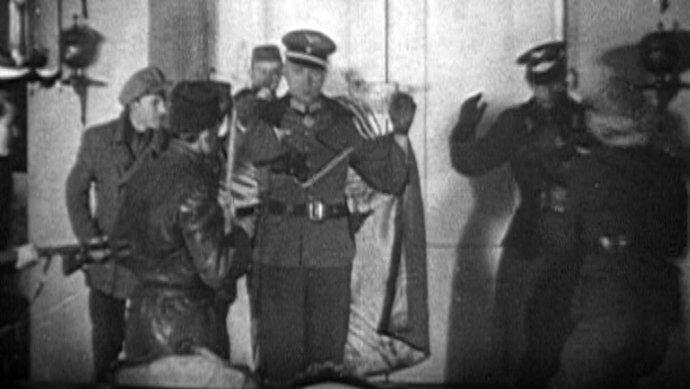 Hraná scéna z filmu Oddíl Chřiby. Muž v plášti a se zvednutýma rukama představuje německého generála Dietricha von Müllera. Repro: film Oddíl Chřiby, ÚSTR a Aleš Macháč