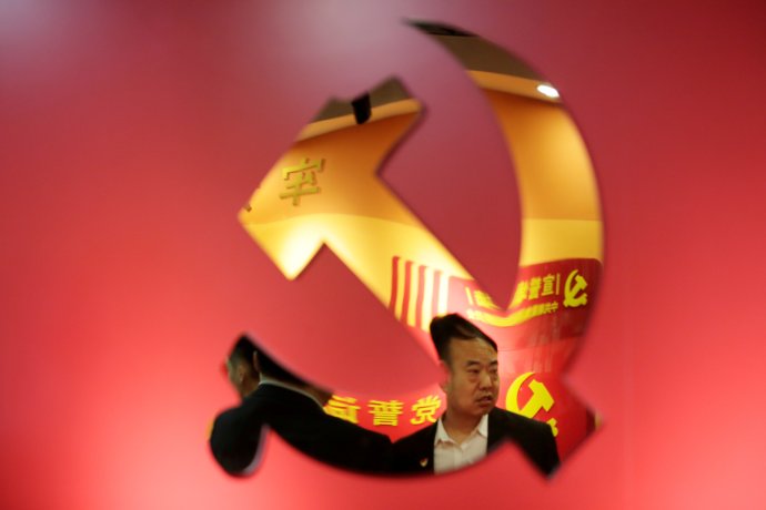 Zdeformovaný odraz člena Komunistické strany Číny se odráží v logu strany. Čína čelí nejhlubší krizi za poslední roky. Foto: Jason Lee, Reuters