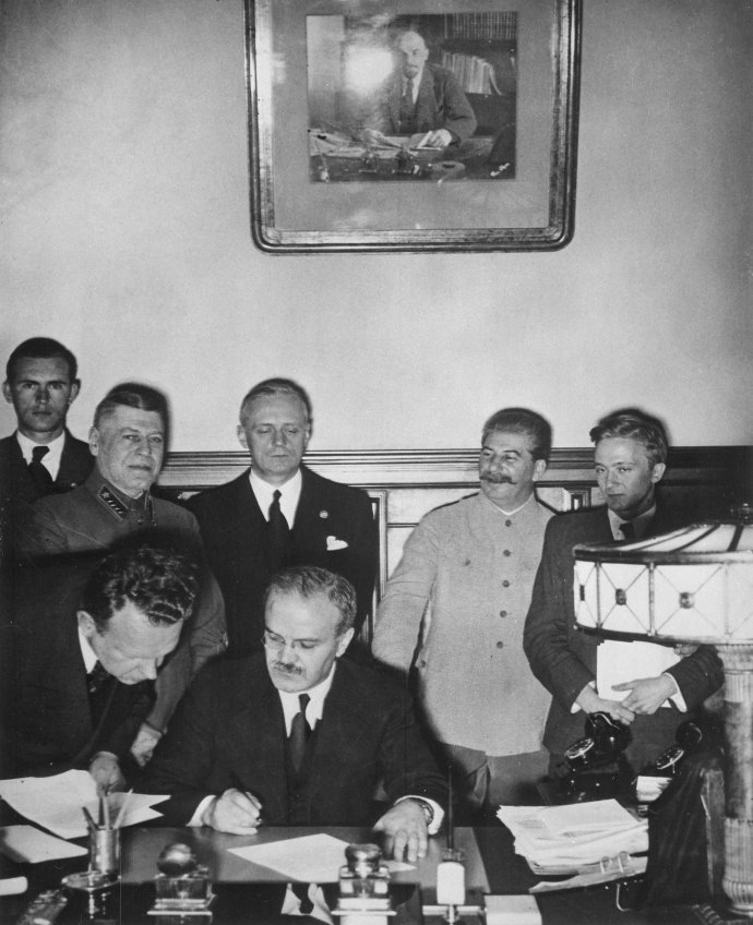 Podpis druhého tajného dodatku smlouvy o neútočení mezi Německem a Sovětským svazem, přezdívané pakt Molotov–Ribbentrop, v moskevském Kremlu 28. září 1939 (smlouva a první tajný dodatek rozdělující východní Evropu mezi Německo a SSSR byly podepsány 23. srpna 1939). Hitlerův ministr zahraničí Joachim von Ribbentrop stojí třetí zleva, vedle něj je Josif Vissarionovič Stalin. Sovětský ministr (lidový komisař) zahraničí Vjačeslav Molotov dokument podepisuje. Foto: autor neznámý, NARA.gov