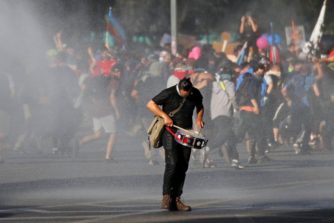Demonstrant bubnuje během policejního zásahu vodním dělem proti protivládním protestujícím v Santiagu de Chile. Foto: Edgard Garrido, Reuters