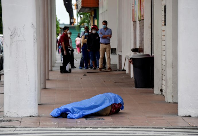 Tělo muže, který zkolaboval patrně na následky nákazy covid-19. Za ním obyvatelé ekvádorského Guayaquilu čekají ve frontě před obchodem. Foto: Vicente Gaibor del Pino, Reuters