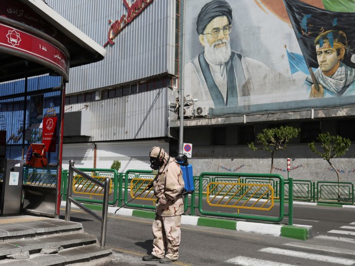 Dobrovolník polovojenské organizace Basídž-e Mostazafín v Teheránu v dubnu 2020 v okolí autobusové zastávky pod dohledem nejvyššího vůdce ajatolláha Chameneího v ochranném obleku bojuje s virem SARS-CoV-2. Foto: Alí Chara, WANA / Reuters
