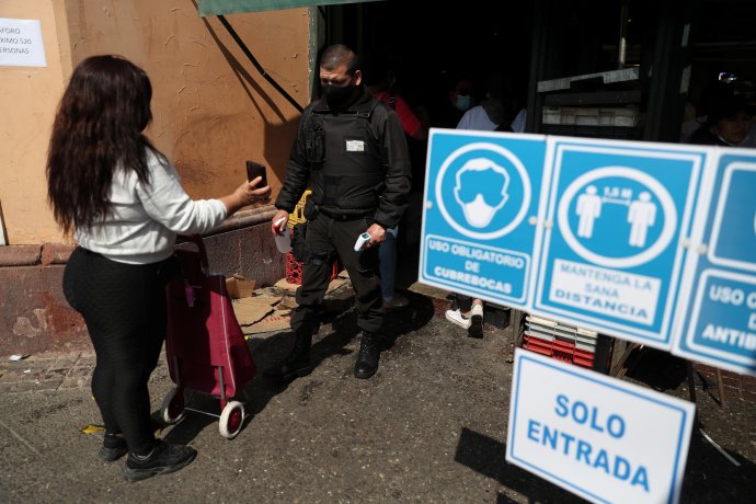 Ochranka u vstupu na tržiště v Santiagu de Chile vedle cedulí o epidemických opatřeních kontroluje zákaznici údaje o očkování v mobilu. Foto: Ivan Alvarado, Reuters