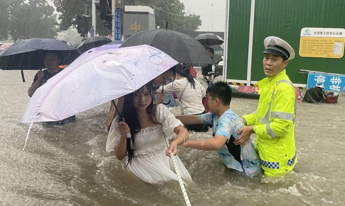 Ulice v dvanáctimilionovém Čeng-čou, úterý 20. července 2021. Přívalový déšť neustává a dopravní policista se snaží lidem pomoci přejít přes zaplavenou ulici. Foto: Reuters