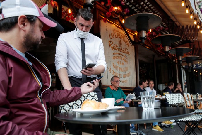 Zákazník v pařížské kavárně ukazuje číšníkovi se staženou rouškou svůj covidový pas. Srpen 2021. Foto: Benoit Tessier, Reuters