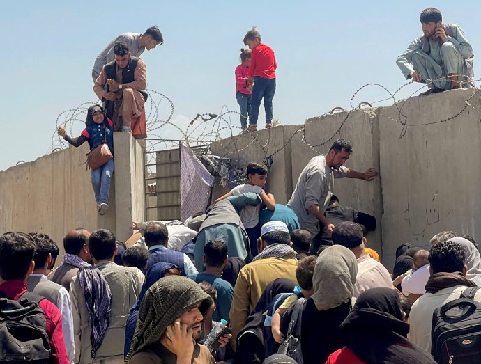 Zoufalí lidé se tlačí před zdí kolem letiště v Kábulu. Mladík vlevo se snaží vytáhnout malou dívku nahoru: tak, aby se oba dostali dovnitř, do areálu letiště. Foto: Reuters
