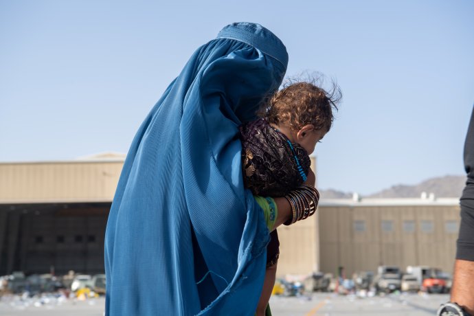 Žena v burce nese dítě na letišti Hamida Karzaího v Kábulu. Je jednou z těch šťastlivých, kterým se podařilo z Afghánistánu na poslední chvíli uprchnout. Ve čtvrtek ovládly letiště výbuchy a přestřelky. Foto: Master Sgt. Donald R. Allen, Reuters