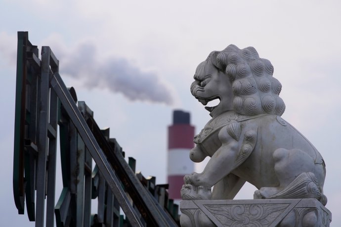 Šanghaj, říjen 2021. Komín uhelné elektrárny chrlí dým plný splodin; v popředí to pozoruje soška strážného lva. Ten v čínské tradici chrání domov před neblahými vlivy zvenčí; uhlíkové emise však zastavit neumí. Foto: Aly Song, Reuters