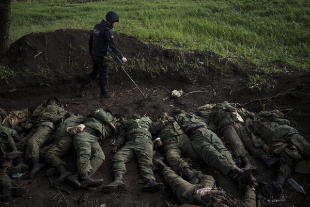 Ukrajinský vojenský pyrotechnik poblíž těl ruských vojáků ve vesnici nedaleko Charkova, kterou opětovně dobyla ukrajinská armáda. Foto: ČTK/AP