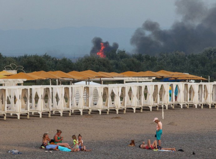 Lidé na pláži na ukrajinském, Ruskem okupovaném Krymu, v pozadí kouř výbuchů na ruské letecké základně u Novofedorivky. Foto: Reuters