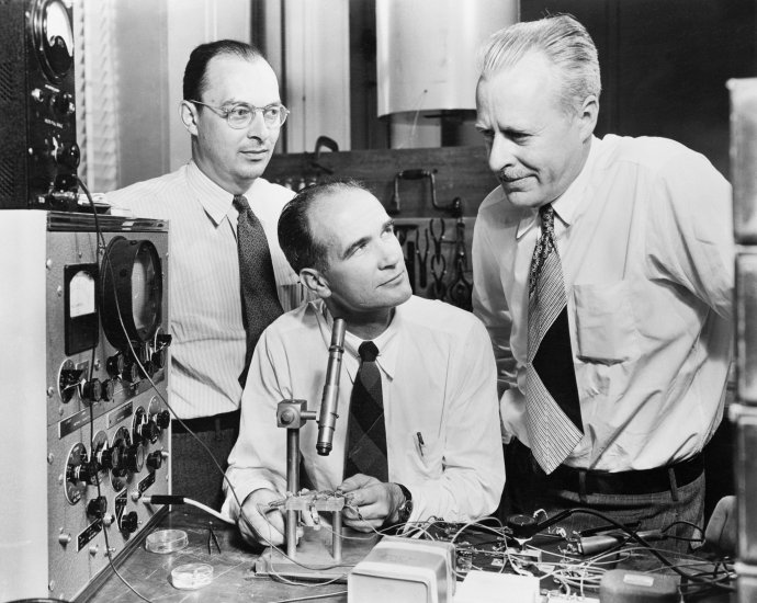 Zleva: John Bardeen, William Shockley a Walter Brattain. Před nimi původní hrotový tranzistor, na kterém se Shockley nepodílel. Foto: AT&T, public domain