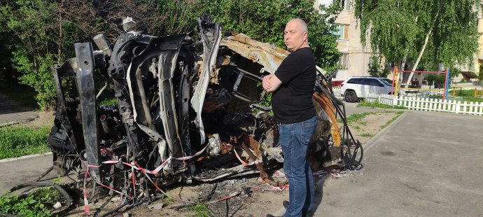 Alexandr Dolenko stojí před vrakem auta, které zničilo ruské bombardování. Foto: archiv rodiny