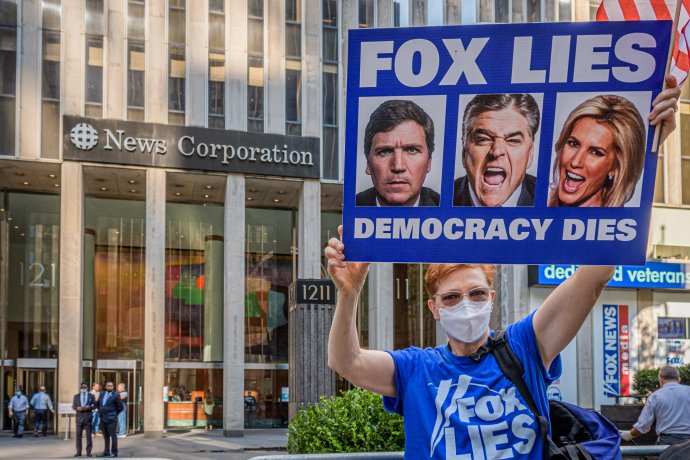 „Fox lže, demokracie umírá,“ hlásí transparent ženy, která v New Yorku protestuje před budovou televize Fox. Na jejím plakátu jsou všichny tři nejsledovanější moderátoři: Tucker Carlson, Sean Hannity a Laura Ingraham. Žaloba zveřejnila jejich údajné konverzace, které podle ní ukazují, že konspiracím o volebních podvodech sami nevěřili - přesto je tvrdili svým divákům. Foto: Erik McGregor, Sipa/Reuters