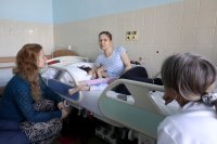 Karolína, která je na posteli se svou dcerou Natálkou, si povídá s nemocniční kaplankou Doubravkou Vokáčovou. Foto: Ludvík Hradilek, Deník N